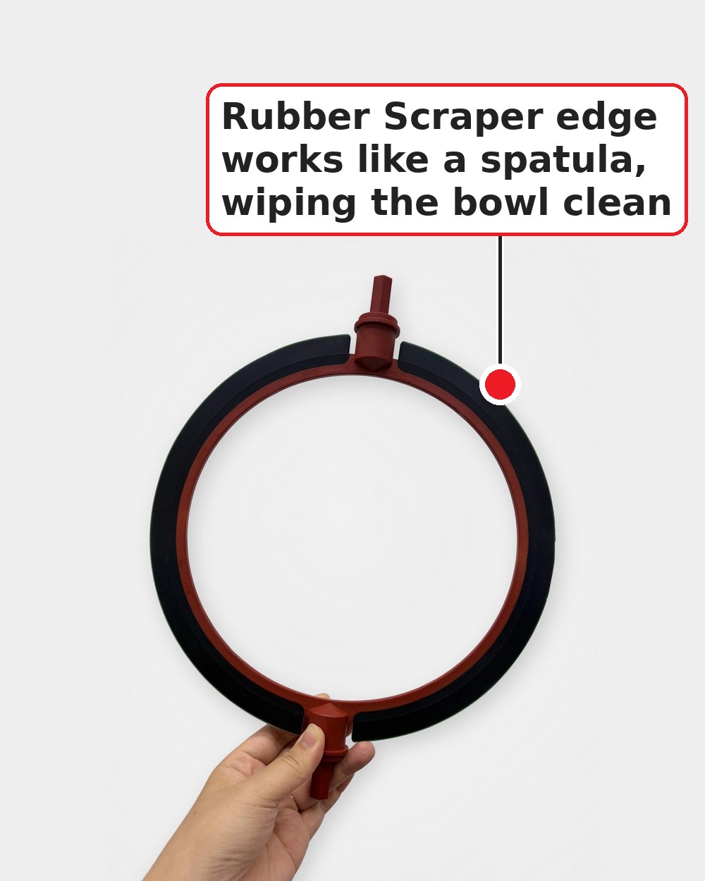 A hand holding The Scraper paddle by its lower shaft: a red ring-shaped frame with charcoal rubber scraper edges along its outer edge, against a white background. Label pointing to the rubber edge: Rubber Scraper edge works like a spatula, wiping the bowl clean.